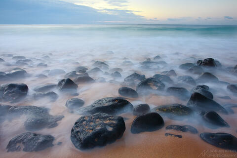 Long exposure dreamy photo from the south shore of Kauai Hawaii on a sandy beach with large rocks and waves. 