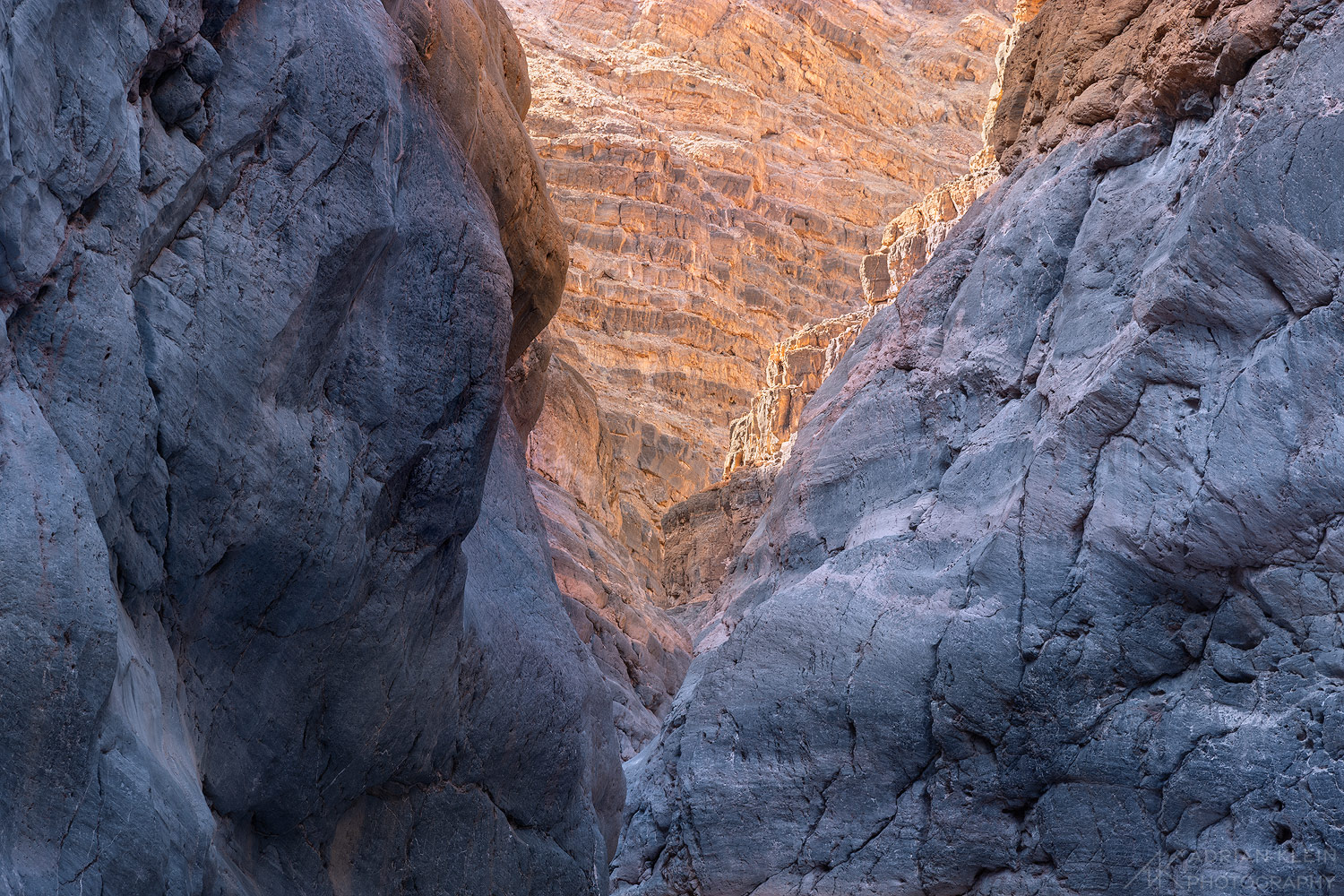 The bottom of a canyon sits in the cool shade as the bright warm sun hits high above in Death Valley National Park.