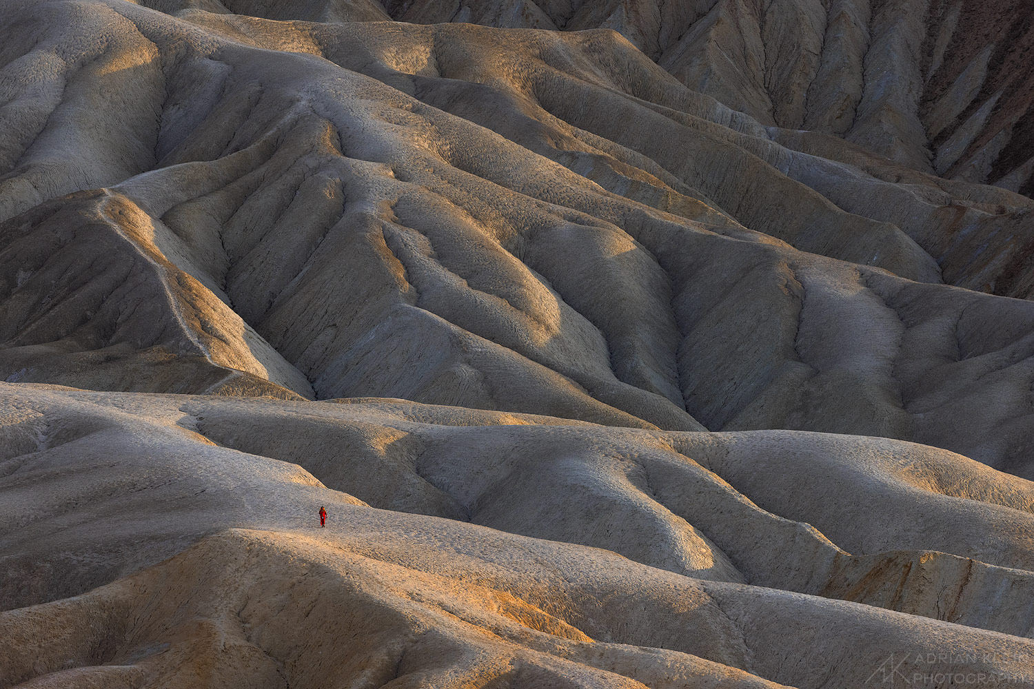 A lone female hiker wearing a red dress taking in the last of the sun as it sets for the day in Death Valley National Park. I...