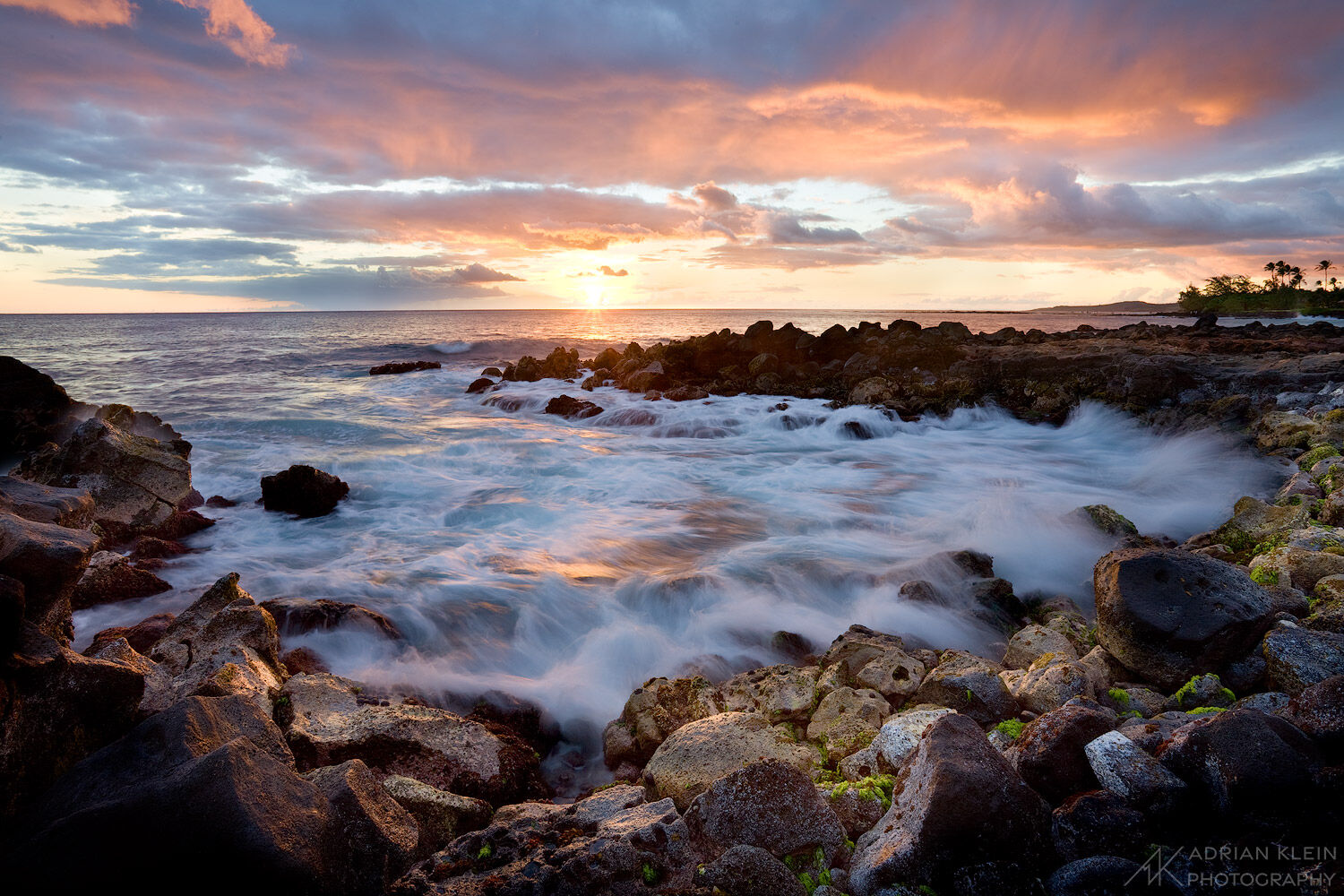 The sun sets along the South Shore of Kauai as the waves roll in over the rocky shore on this Hawaiian Island.