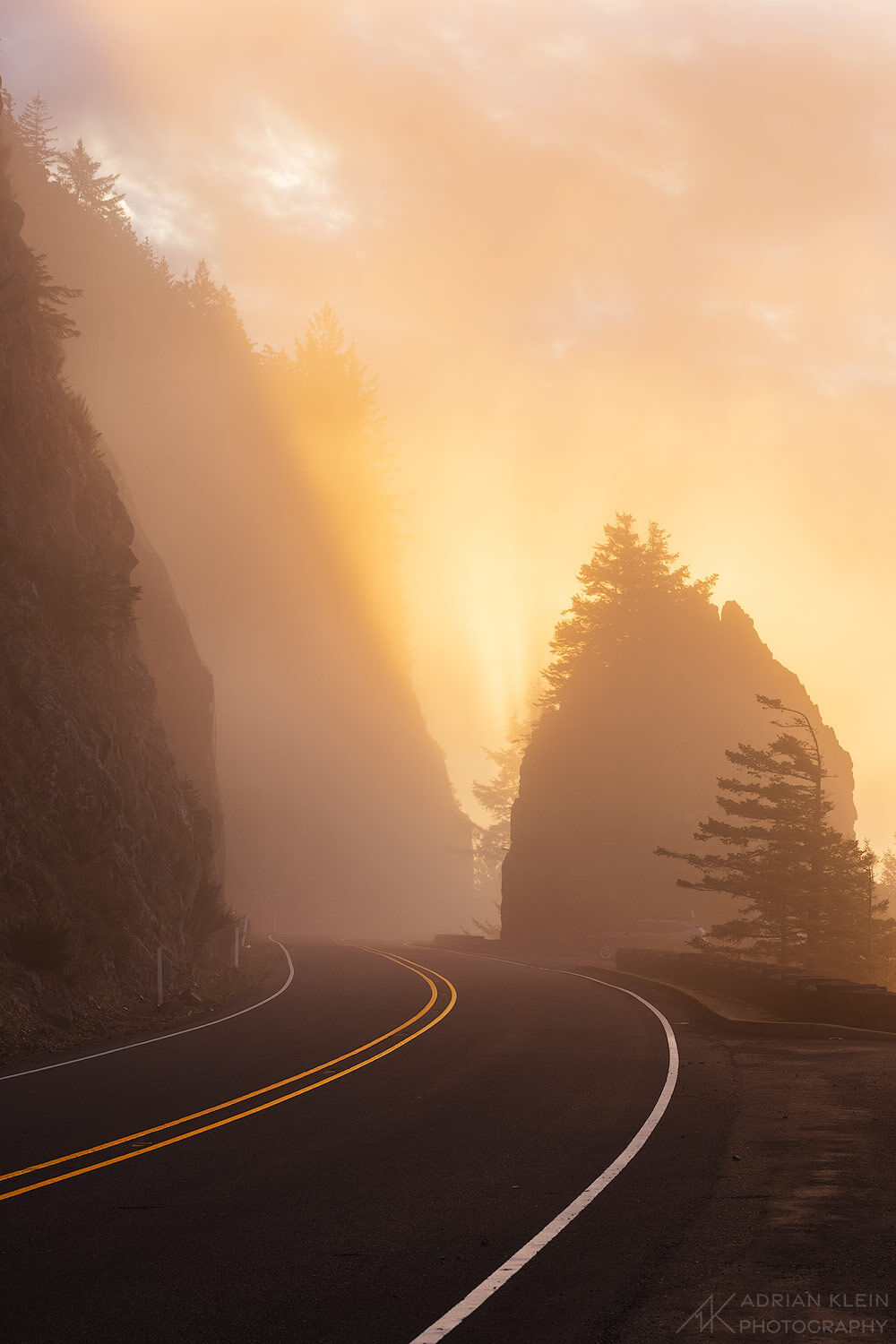 Fog runs up and over the cliffside just as the morning sun pierces through for a fiery glow to the sky. North Oregon Coast. Limited...