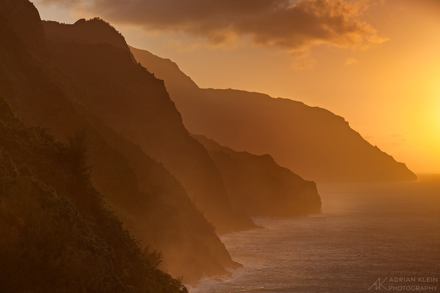 The sun glows intensely through the ocean air and clouds along the rugged Napali Coast of Kauai, Hawaii. Limited Edition of 100...