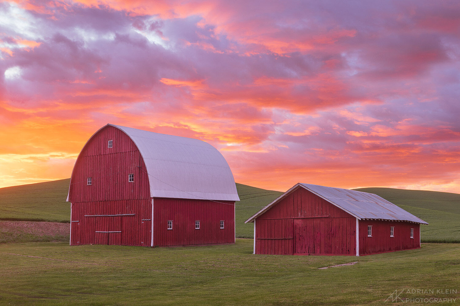 A picturesque red barn and rolling green hills during a very colorful sunset. Eastern Washington in the Palouse Hills region....