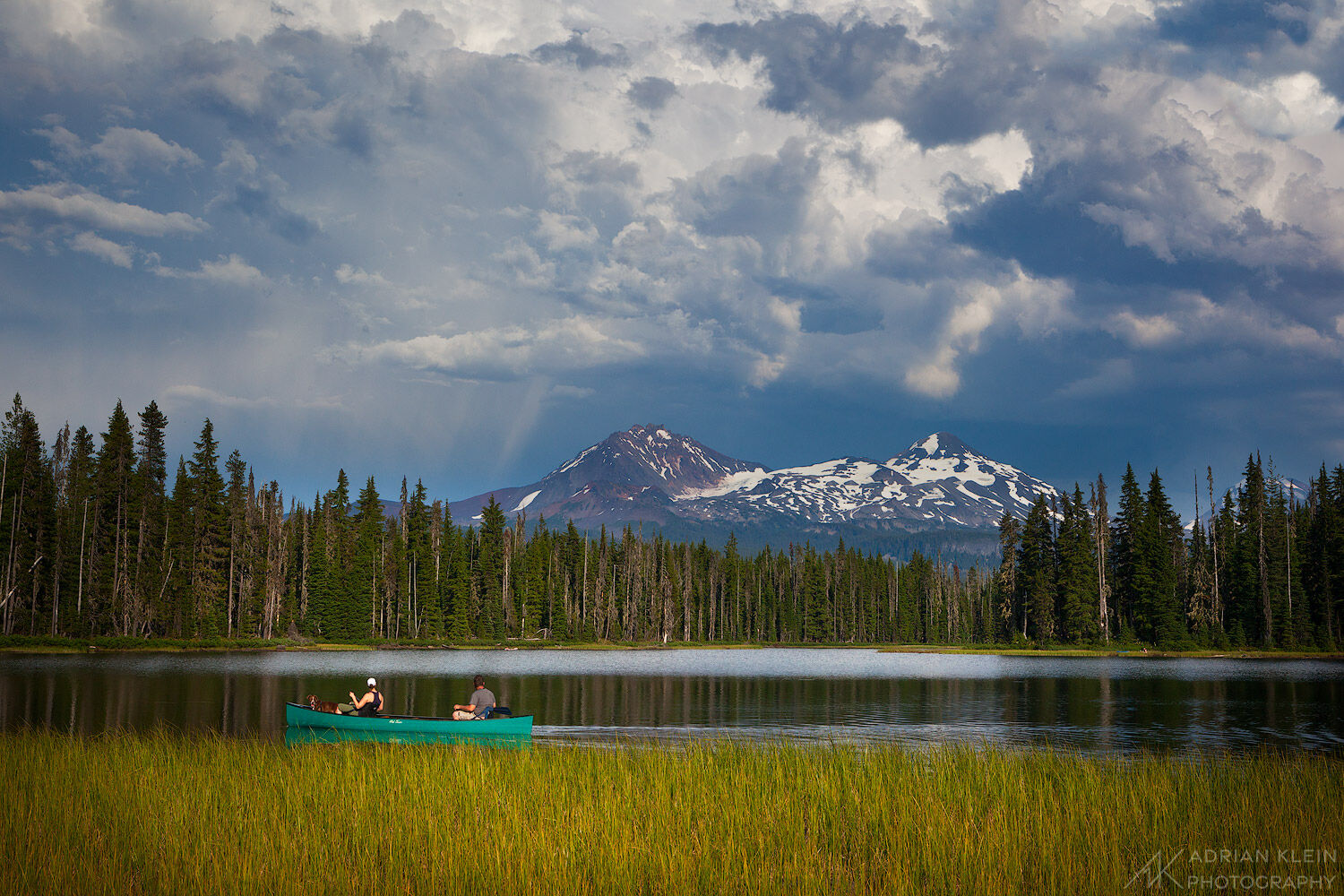 Two people and a dog canoeing on peaceful Scott Lake in Central Oregon as a stormy sky brews above.