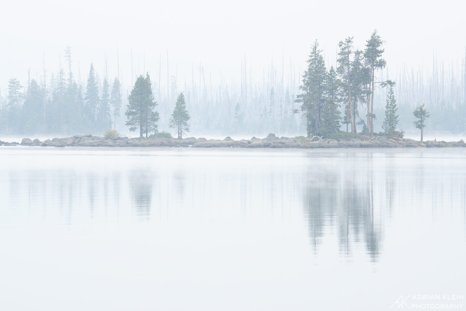 A small island sits in front of a forest burned in years past. Sky is filled with fog and smoke from a near by fire. Limited...